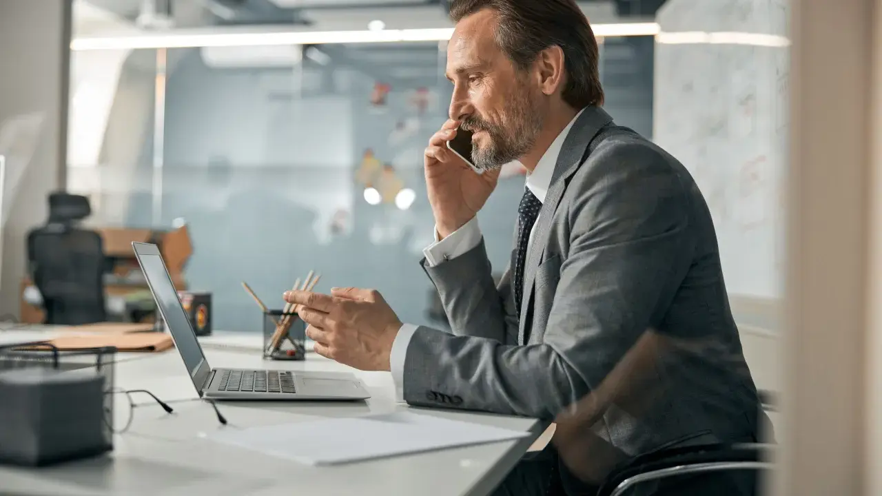 Mężczyzna w garniturze rozmawia przez telefon, pracując przy laptopie. Zastanawia się, co oznacza skrót CEO.