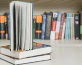 Otwarty podręcznik Excel stoi na stosie książek. Na półce za nimi widać wiele innych tytułów.