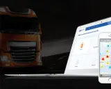 Pomarańczowa ciężarówka obok laptopa i telefonu z mapą pokazującą lokalizację pojazdów dzięki systemowi GPS.