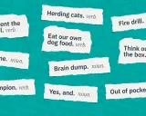 Karty z wyrwanymi fragmentami tekstu, prezentujące popularne **buzzwordy po polsku**, takie jak "Reinvent the wheel" czy "Think outside the box".