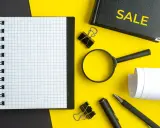 Notatnik, lupa, długopis i zeszyt z napisem "SALE" – narzędzia do analizy i strategii cross selling.