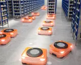 Pomarańczowe roboty autonomiczne poruszają się między rzędami regałów w nowoczesnych magazynach, usprawniając logistykę.