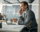 Mężczyzna w garniturze rozmawia przez telefon, pracując przy laptopie. Zastanawia się, co oznacza skrót CEO.