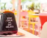 Na serwetniku napis: "Keep calm and eat gelato". W tle kolorowe krzesła, idealne na letnie hasła promocyjne.