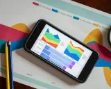 Smartfon z wykresem na ekranie, obok kredki i szkło powiększające. Analiza danych, jak funkcja filtruj Excel.