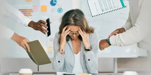 Kobieta z rękami na skroniach, przytłoczona zadaniami. Brak organizacji pracy własnej prowadzi do stresu i chaosu.