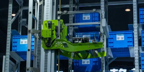 Automatyczny magazyn z niebieskimi pojemnikami. Zielony mechanizm pobiera jeden z nich. To przykład, co to jest telemetria w działaniu.