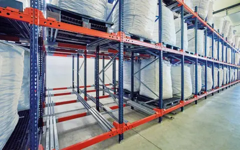 Magazyn z workami wypełnionymi materiałem, ułożonymi na paletach w regałach. System regałów jezdnych, wykorzystujący metodę LIFO (Last-In, First-Out), zapewnia optymalne wykorzystanie przestrzeni.