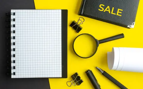 Notatnik, lupa, długopis i zeszyt z napisem "SALE" – narzędzia do analizy i strategii cross selling.
