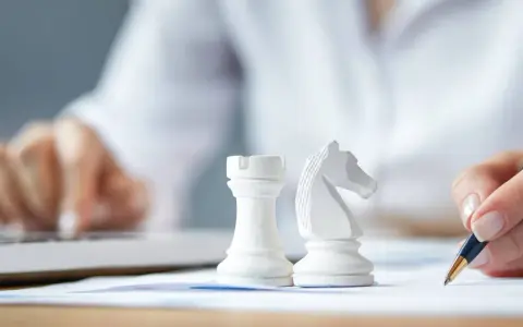 Strategia dla dużych firm: białe figury szachowe, ręka pisząca na papierze, druga ręka na klawiaturze laptopa.