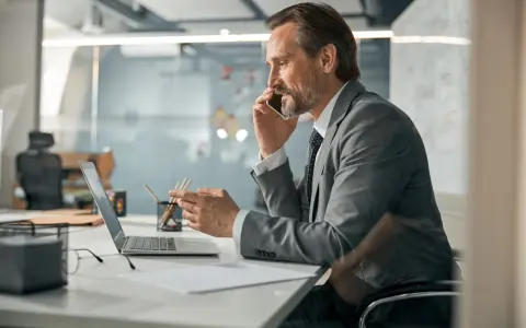 Mężczyzna w garniturze rozmawia przez telefon, pracując przy laptopie. Zastanawia się, co oznacza skrót CEO.