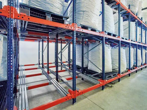 Magazyn z workami wypełnionymi materiałem, ułożonymi na paletach w regałach. System regałów jezdnych, wykorzystujący metodę LIFO (Last-In, First-Out), zapewnia optymalne wykorzystanie przestrzeni.
