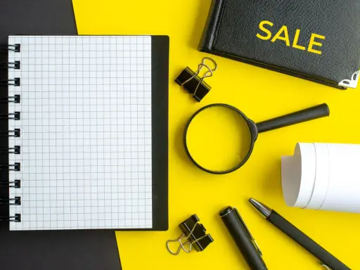 Notatnik, lupa, długopis i zeszyt z napisem "SALE" – narzędzia do analizy i strategii cross selling.