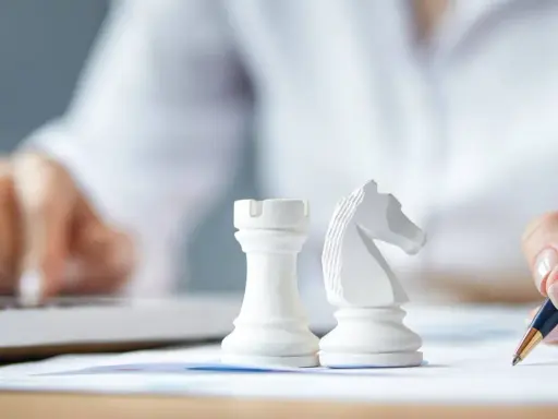 Strategia dla dużych firm: białe figury szachowe, ręka pisząca na papierze, druga ręka na klawiaturze laptopa.