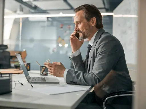 Mężczyzna w garniturze rozmawia przez telefon, pracując przy laptopie. Zastanawia się, co oznacza skrót CEO.