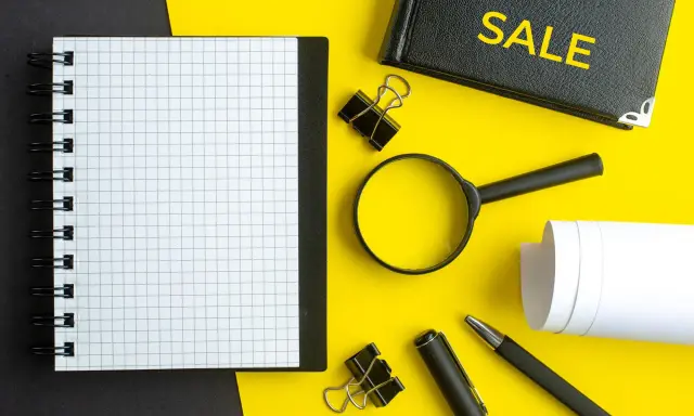 Notatnik, lupa, długopis i zeszyt z napisem "SALE" – narzędzia do analizy i strategii cross selling.