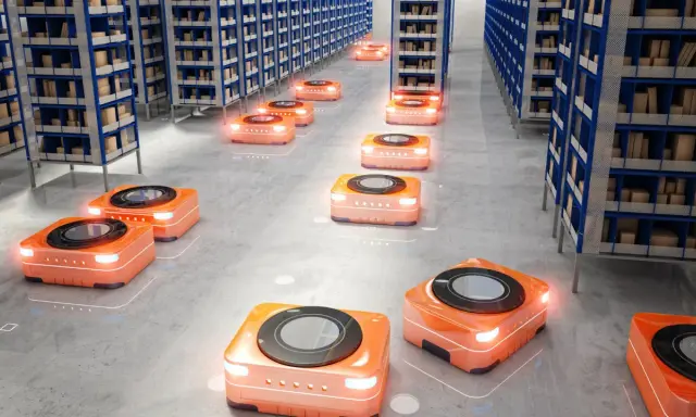 Pomarańczowe roboty autonomiczne poruszają się między rzędami regałów w nowoczesnych magazynach, usprawniając logistykę.