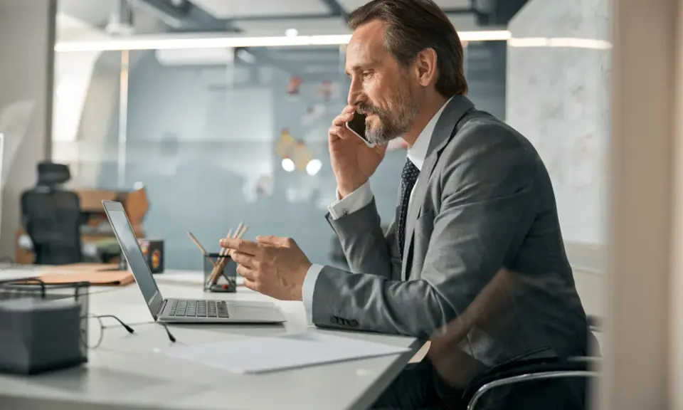 Mężczyzna w garniturze rozmawia przez telefon, pracując przy laptopie. Zastanawia się, co oznacza skrót CEO.