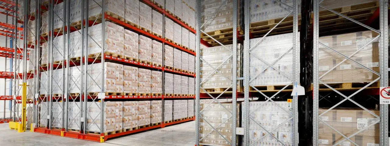Wysokie regały magazynowe wypełnione paczkami na paletach, gotowe do transportu. To przykład prawidłowej instrukcji magazynowania i składowania materiał&oacute;w.